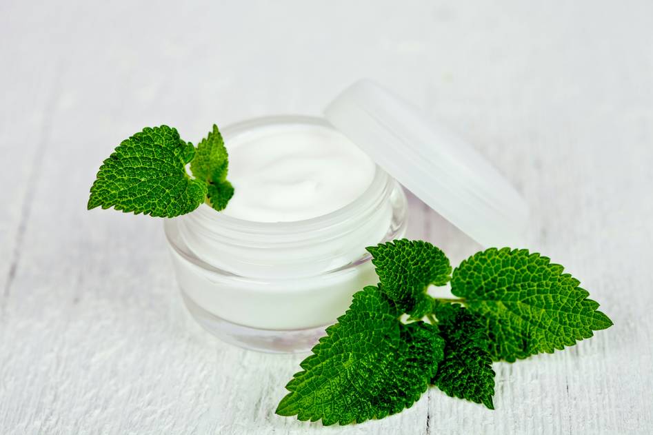 Hand holding fresh aloe vera leaf beside jars of homemade herbal skincare remedies on wooden table