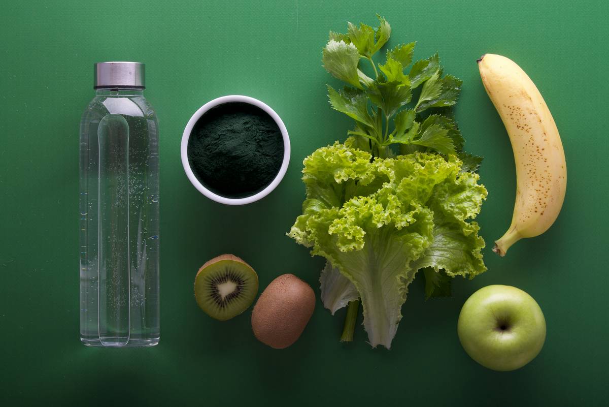 Woman drinking lemon water with fresh greens on wooden table for Detox Support